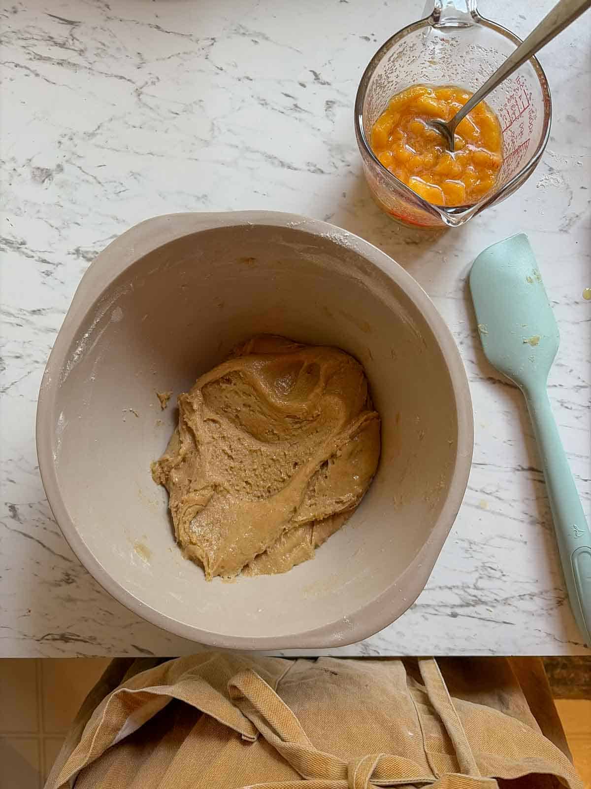 Glossy smooth cookie batter with a glass measuring cup of peaches beside it.