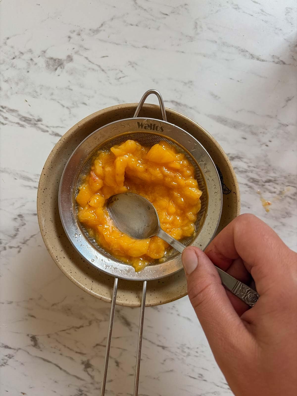 Peaches in a strainer with a spoon pressing them down.