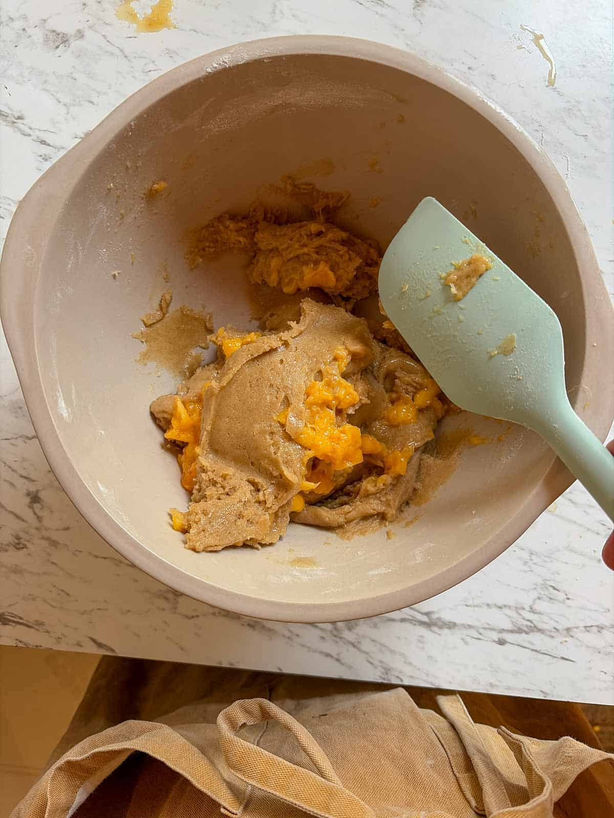 Chunky peach sauce being folded into cookie batter with a spatula.